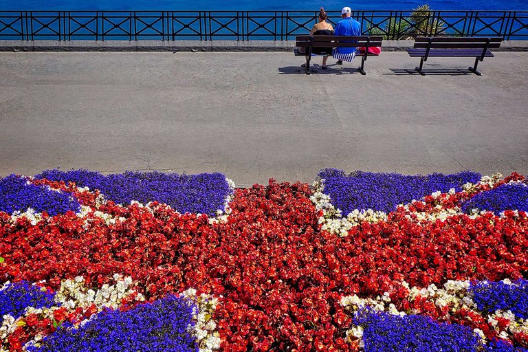 Paar in England vor Blumenrabatte auf einer Bank mit Meerblick