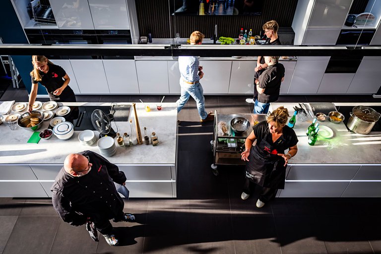 Der Blick von oben auf die Küche, zu sehen sind Steindorf, Neubaur, einige Jugendliche und die Arbeitsplatte mit Essen