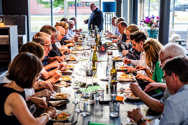 Etwa 20 Menschen verschiedener Generationen sitzen speisend an einer Tafel